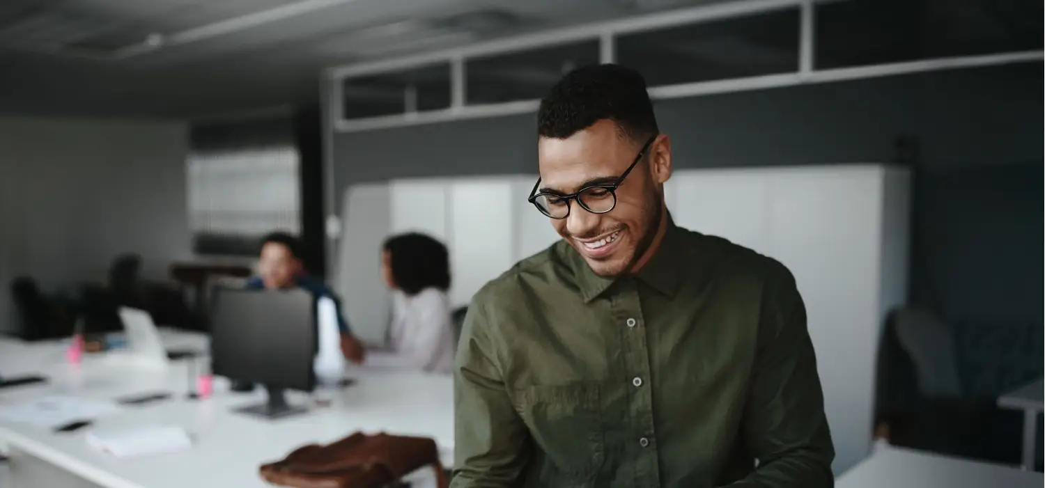 cheerful young businessman using digital tablet smiling while his colleagues working background 1